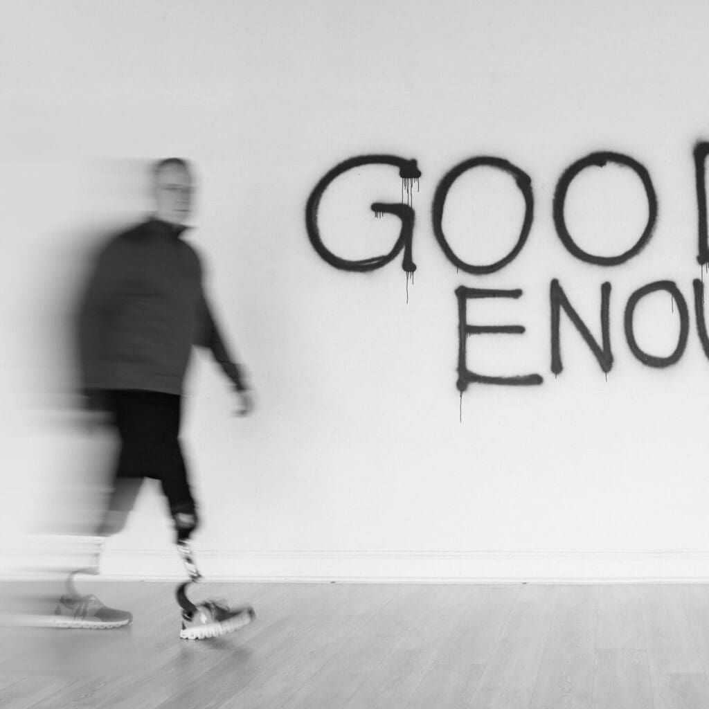 Paul Kent walking along a wall with the words "Good Enough" written on it.